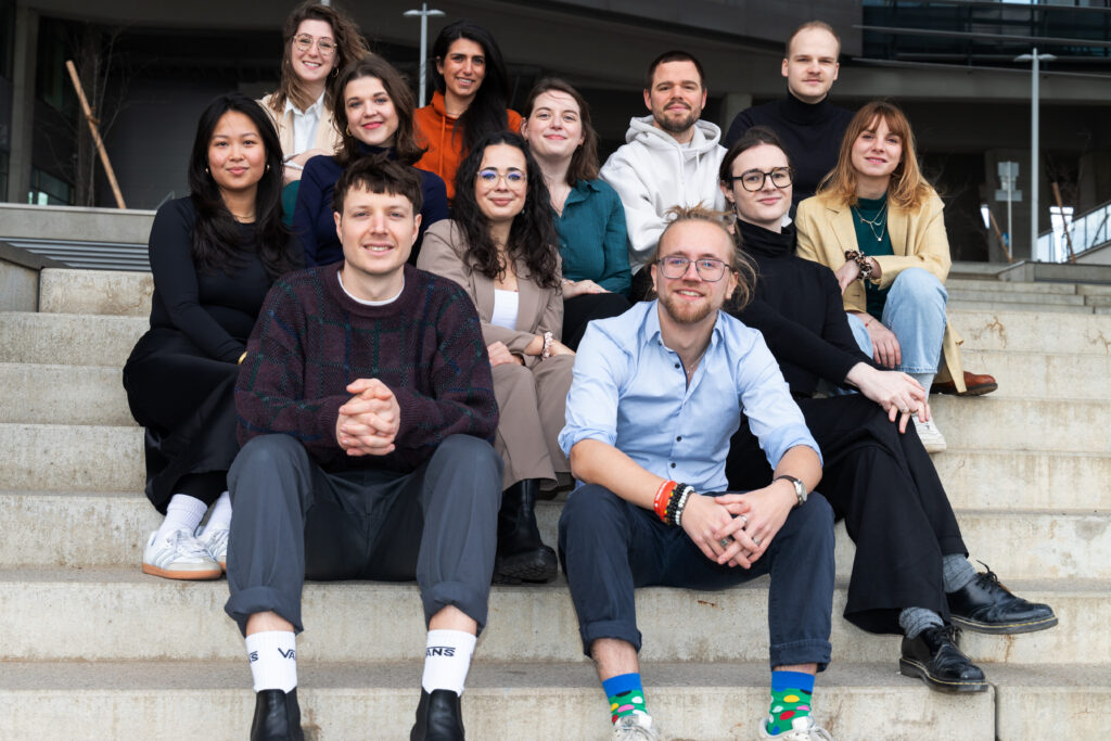 12 Trainees von Durchgang 5 sitzen auf Stiegen verteilt für ein Gruppenfoto.